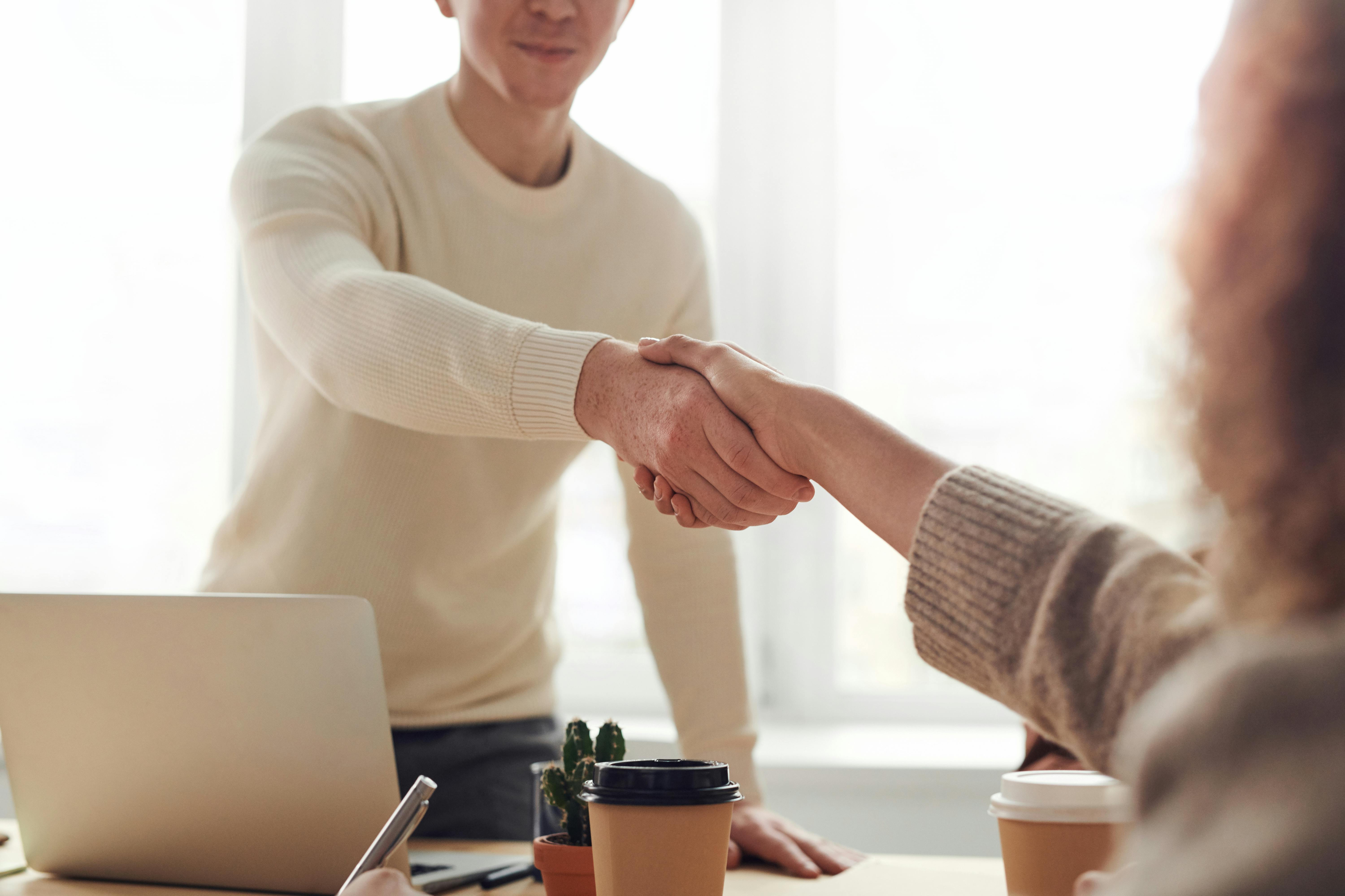 A handshake between two business professionals at a meeting, symbolizing a partnership for a business line of credit in Canada. A laptop, coffee cups, and plants are on the table, representing collaboration with Canada Capital for business financing solutions.